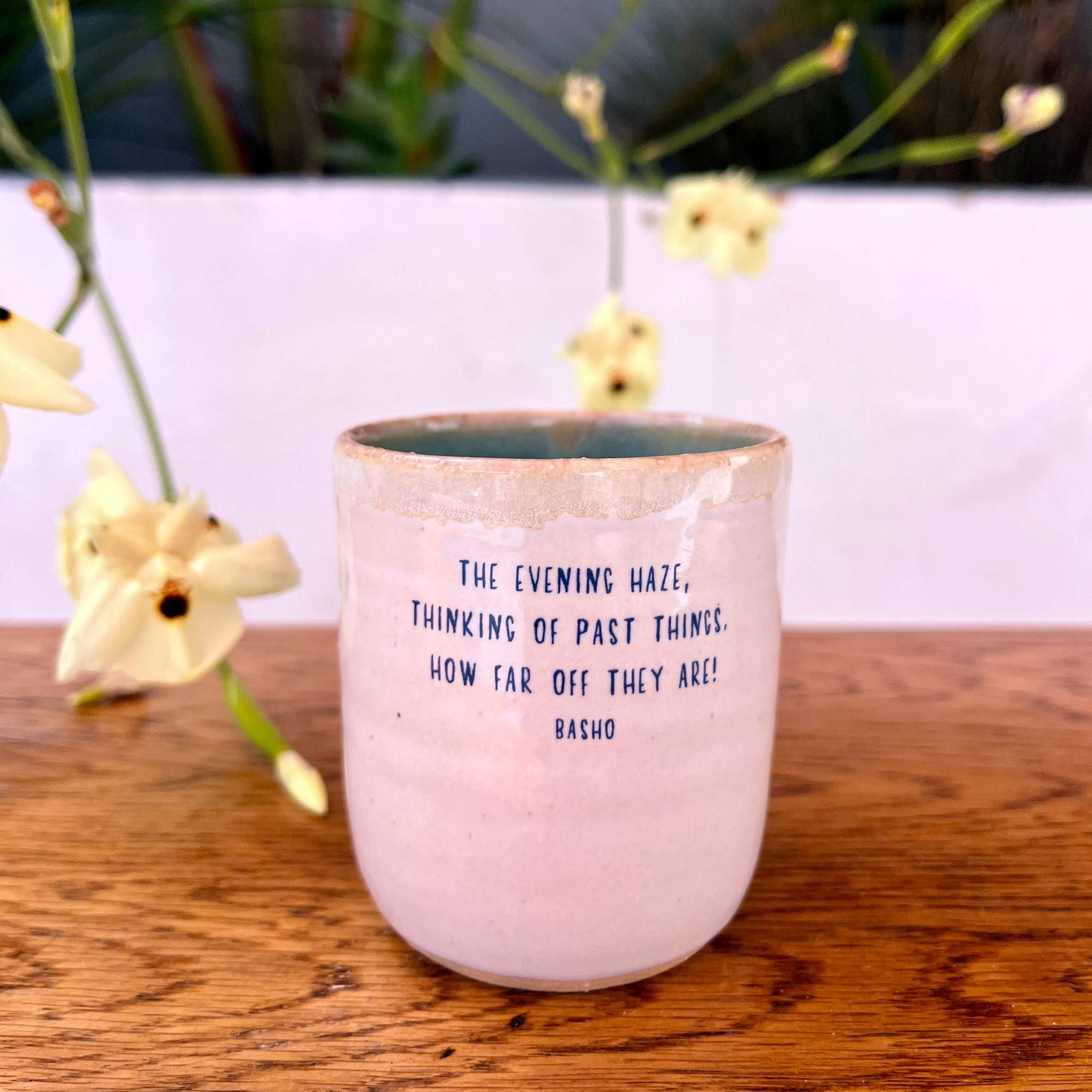 Pink ceramic cup with text on a wooden surface with flowers in the background