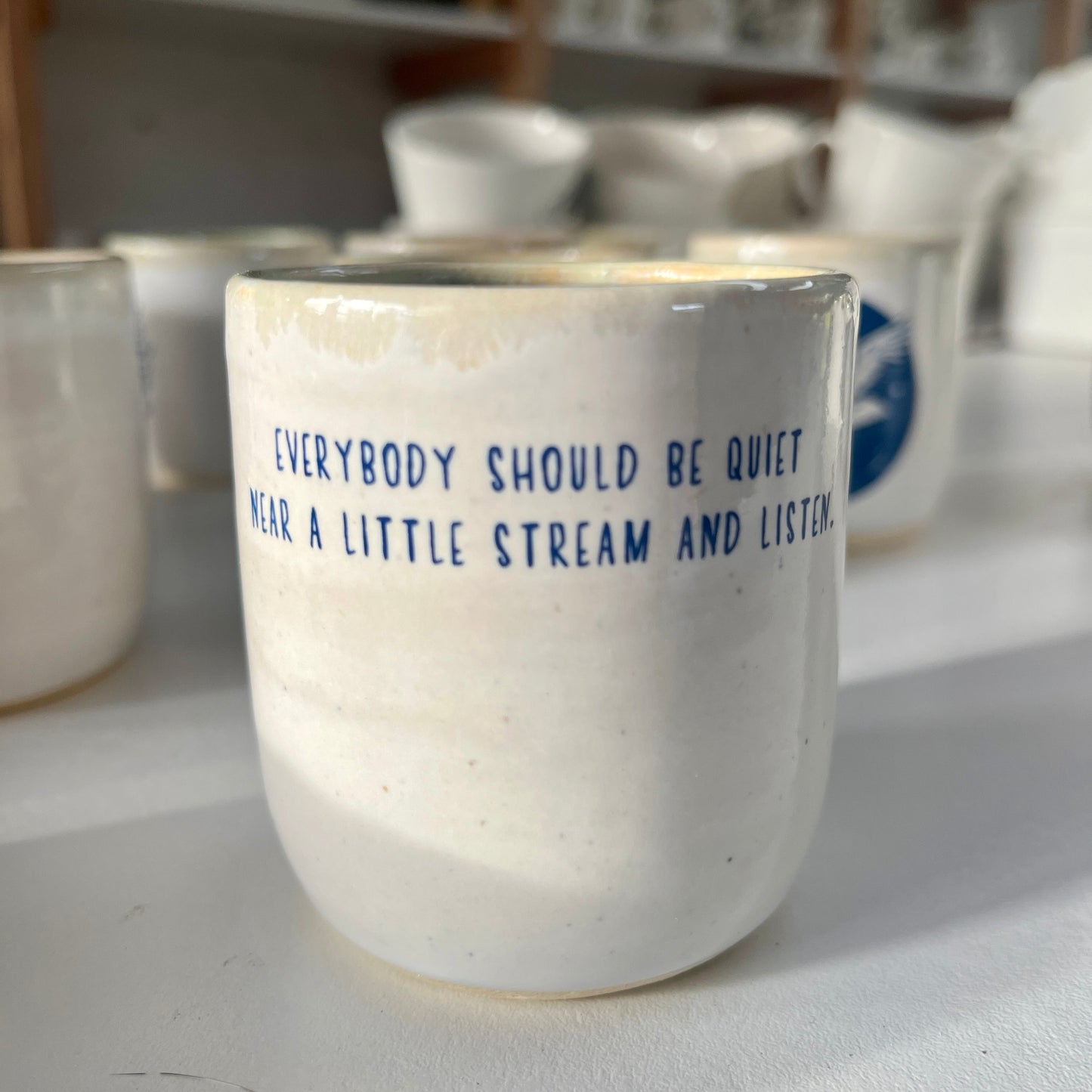 White ceramic cup with blue text in a pottery studio setting