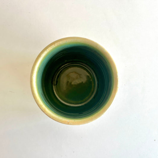 Ceramic cup with green interior and gold exterior on a white background