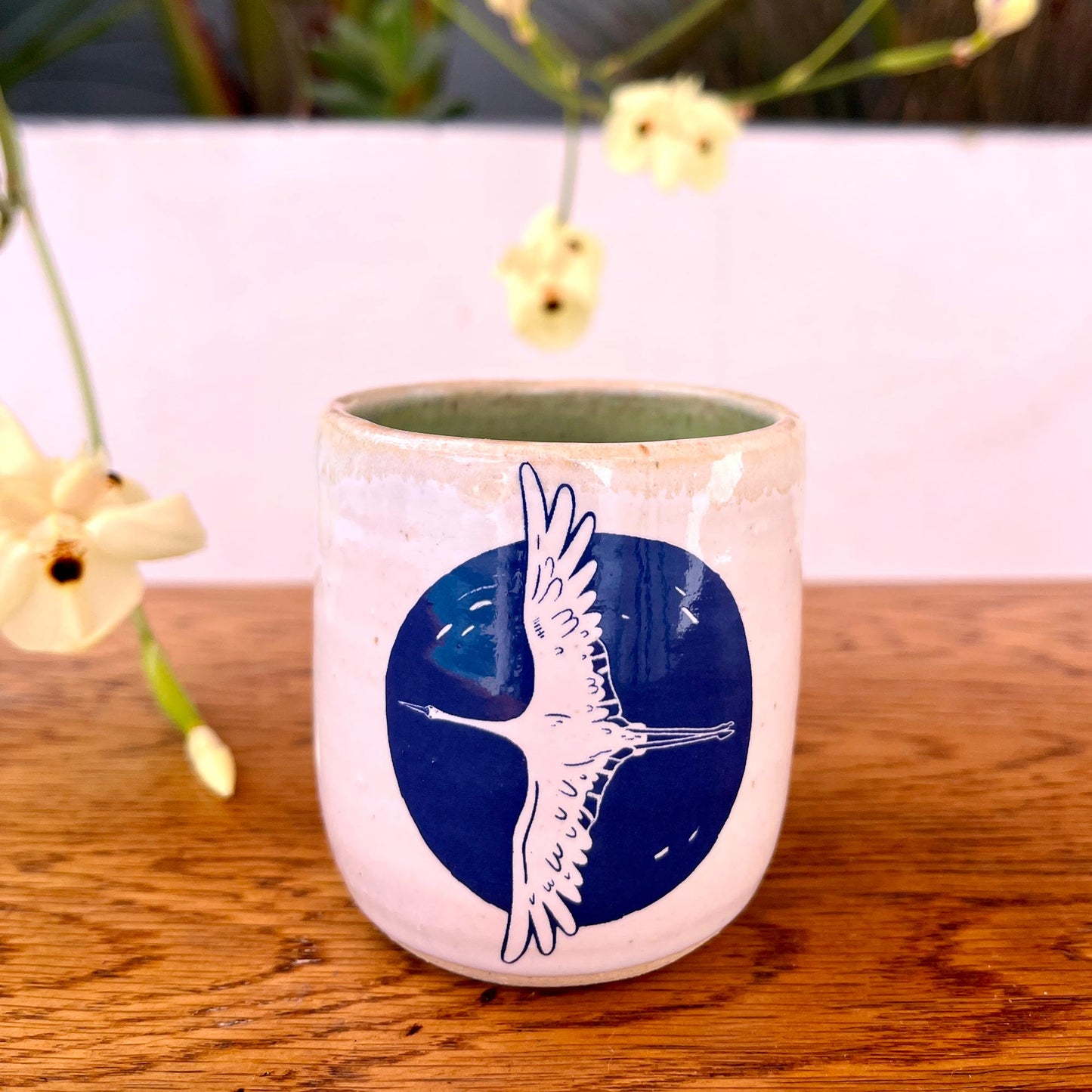 Ceramic mug with blue design of a bird on a wooden surface with flowers in the background