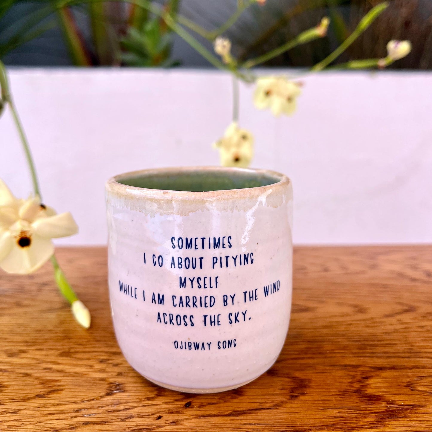 Ceramic mug with a quote on a wooden surface with flowers in the background