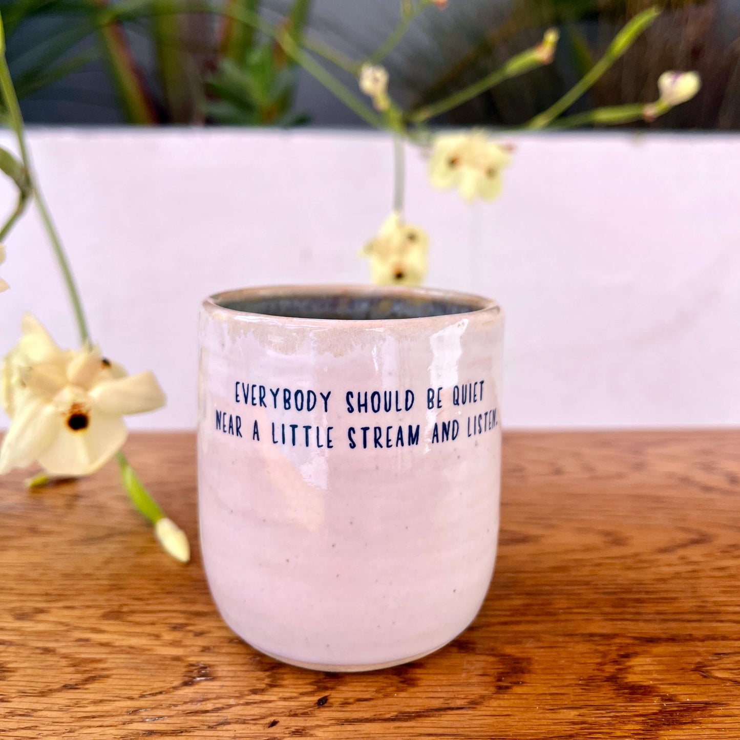 Pink glass mug with text on a wooden surface with flowers in the background