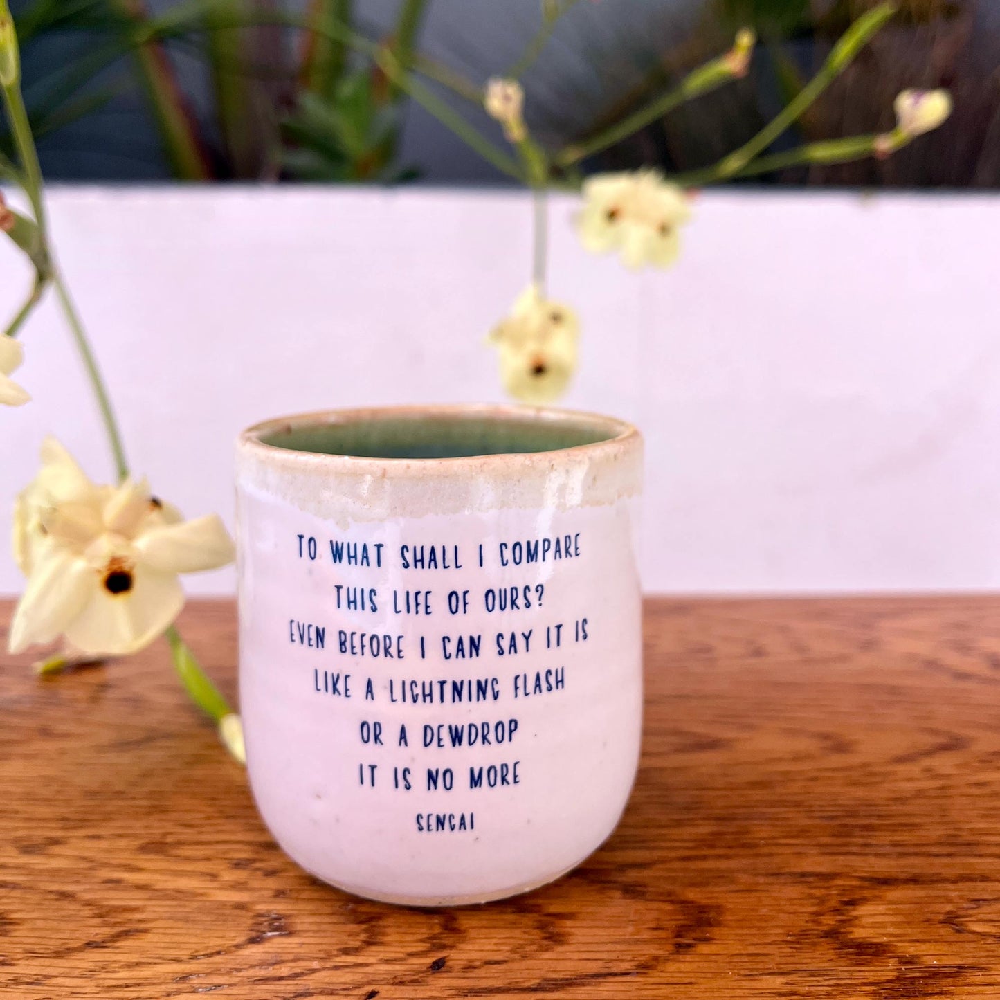 Ceramic mug with a quote on a wooden surface with flowers in the background