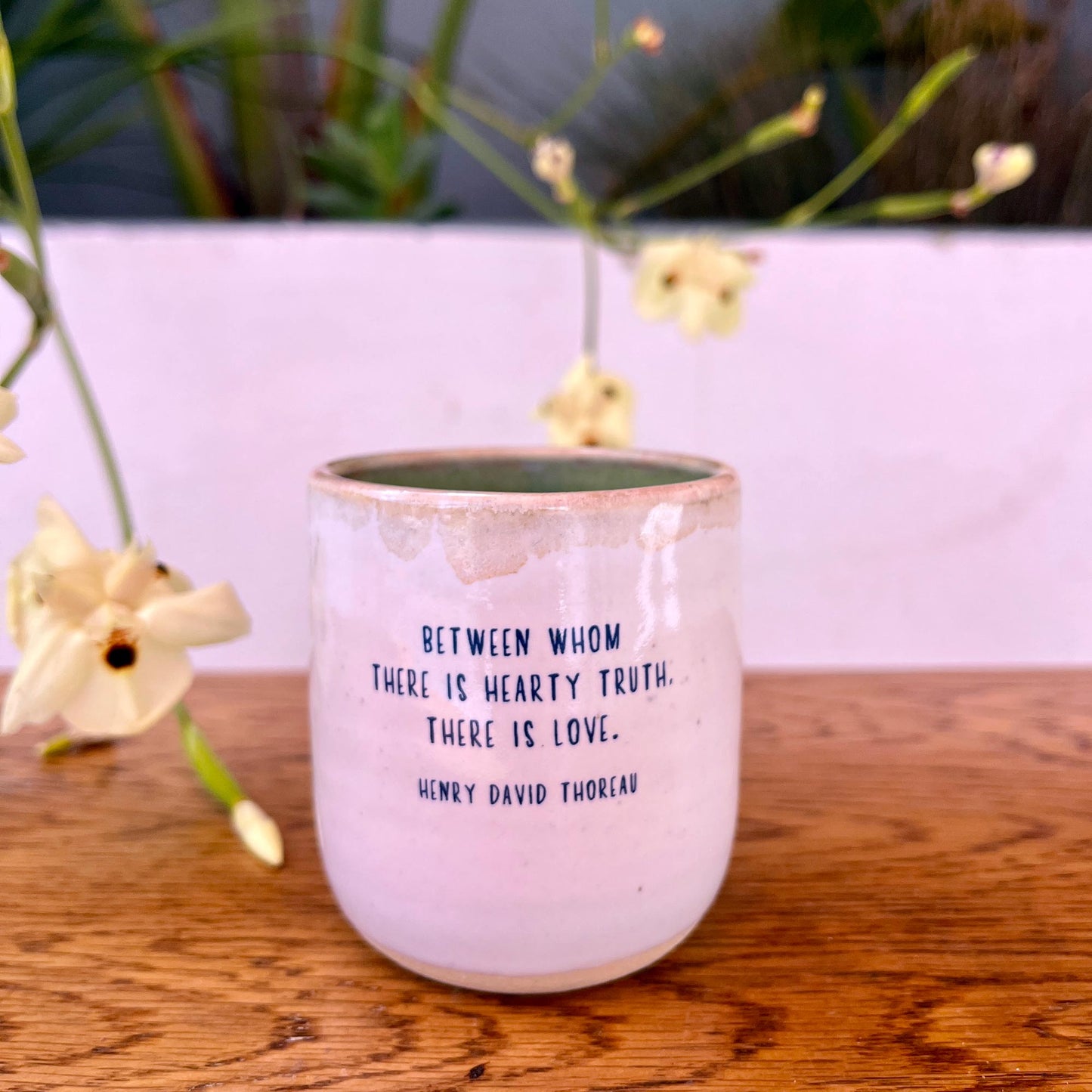 Pink ceramic mug with a quote on a wooden surface with flowers in the background