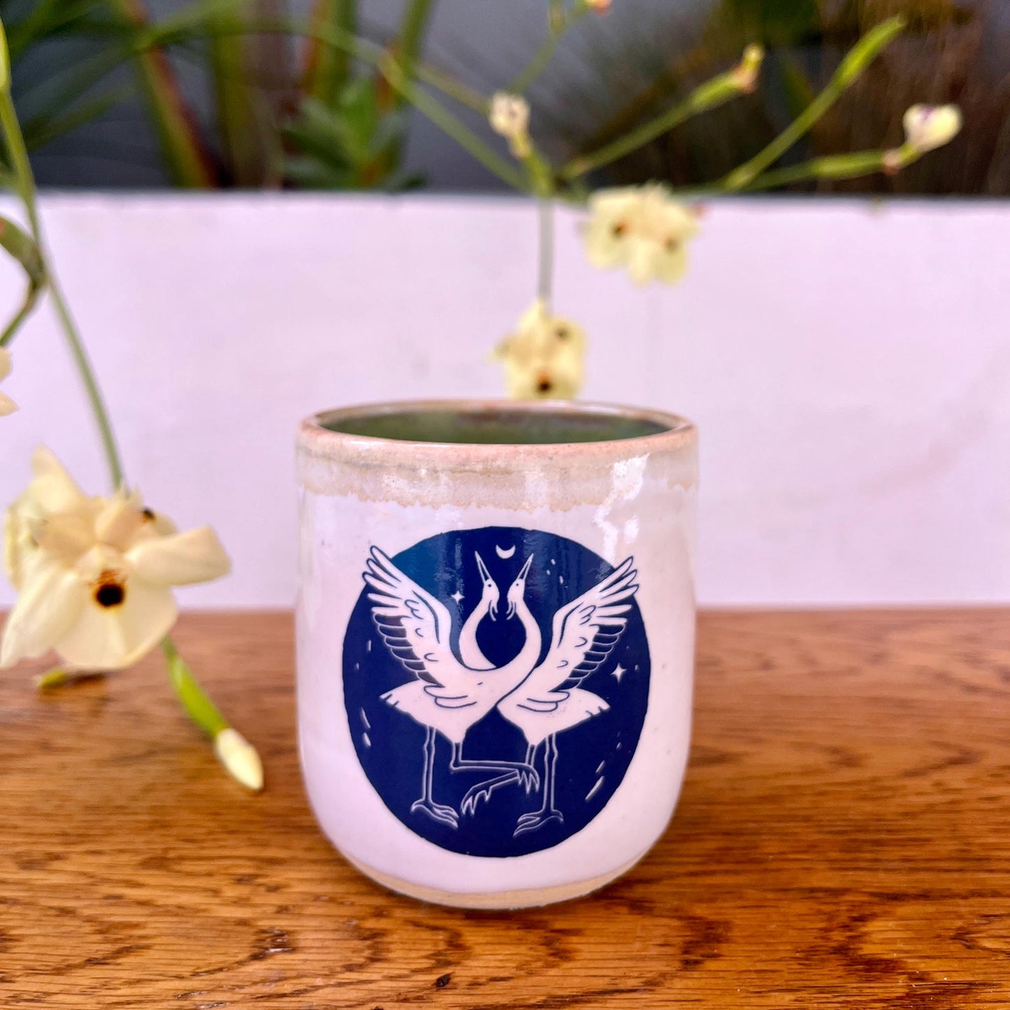 Ceramic tumbler with bird design on a wooden surface with plants in the background