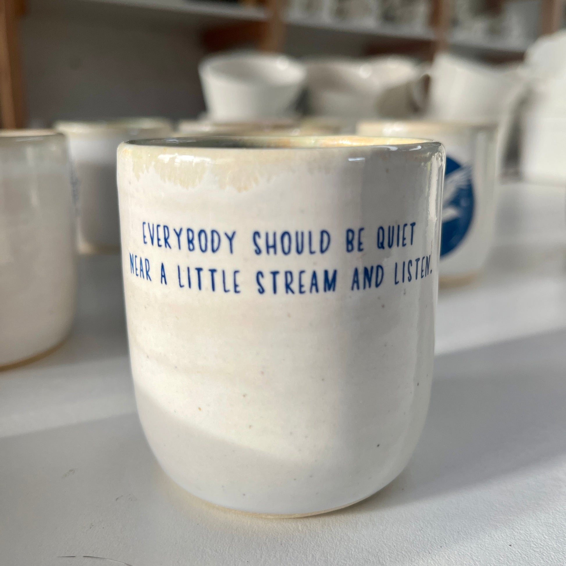 White ceramic cup with blue text in a pottery studio setting